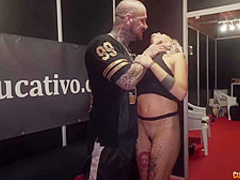 Tattooed man is fucking a slutty blonde babe in a mini skirt, in front of many people