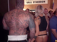 Tattooed man is fucking a slutty blonde babe in a mini skirt, in front of many people